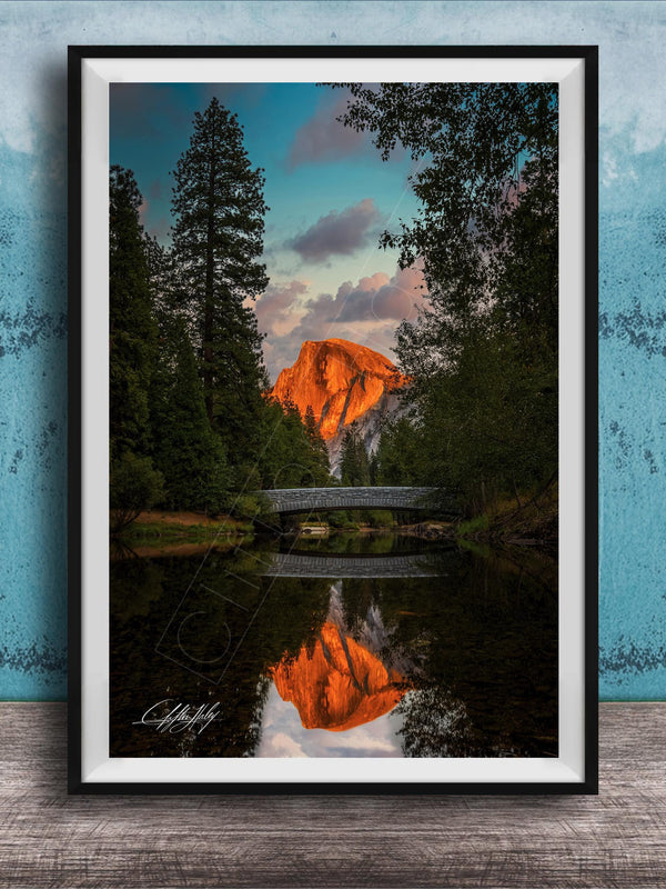 A framed photograph depicting a scenic landscape with a bridge, trees, and a mountain in the background, reflecting in a body of water.