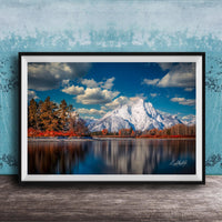 A framed photograph depicting a serene mountain landscape with a calm lake reflecting the surrounding scenery, including trees and mountains in the background.