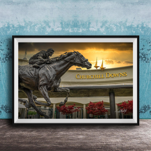 A bronze statue of a jockey riding a horse, with the words "Churchill Downs" displayed above it, against a backdrop of a sunset sky and sailboats.