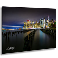 A nighttime cityscape with illuminated skyscrapers and a body of water in the foreground.