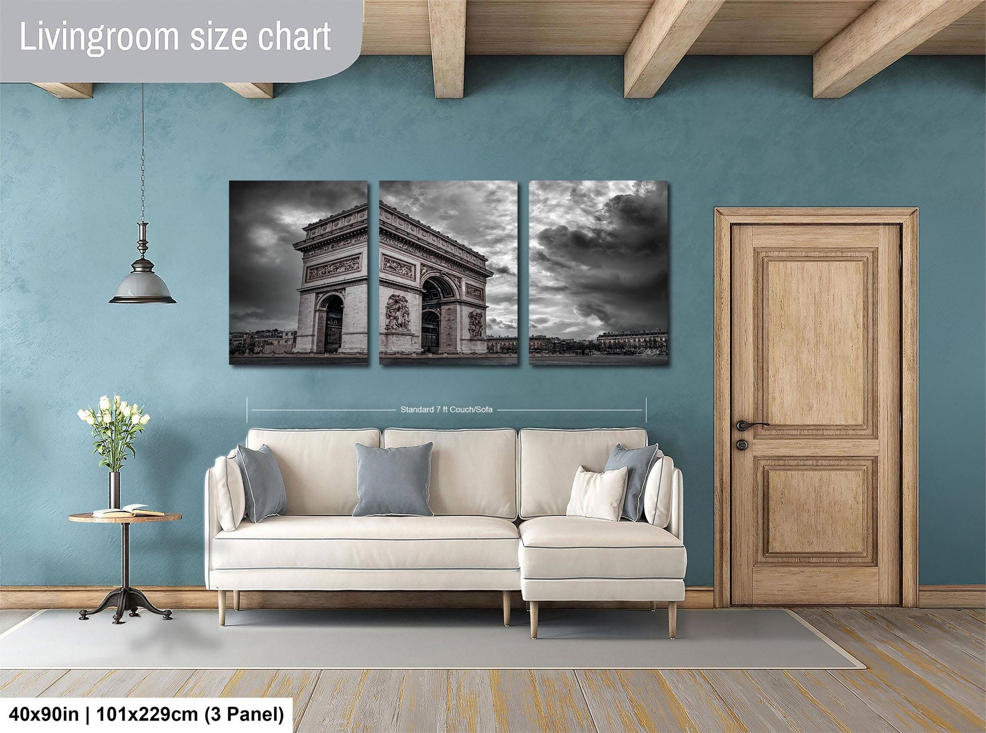 The image is a living room with a large wall art piece depicting the Arc de Triomphe in Paris. The wall art is divided into three panels, with the largest panel covering the entire wall. The living room has a white sofa and a wooden door, and the floor is covered with a gray rug.
