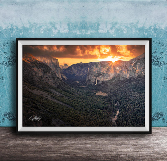 A framed photograph of a breathtaking mountain landscape at sunset, with the sun's rays illuminating the scene and casting a warm glow over the rugged terrain.