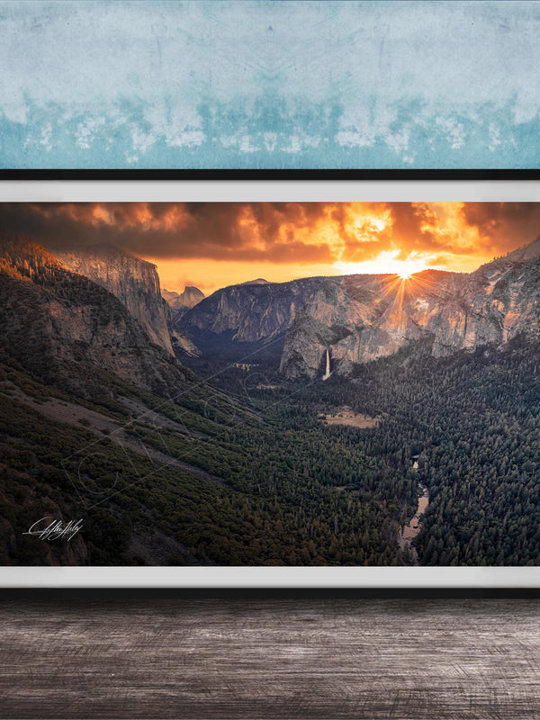 A framed photograph of a breathtaking mountain landscape at sunset, with the sun's rays illuminating the scene and casting a warm glow over the rugged terrain.