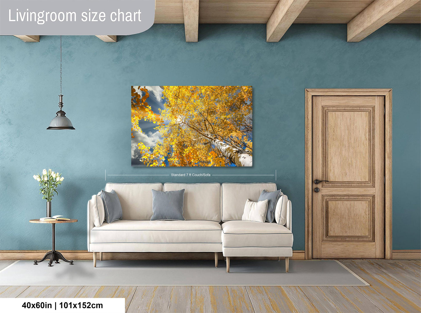 a living room with a large painting of a tree with yellow leaves hanging on the wall. The painting is framed in a white frame and measures 40 inches by 101.5 centimeters. The room has a white sofa, a wooden door, and a wooden table with a vase of flowers.