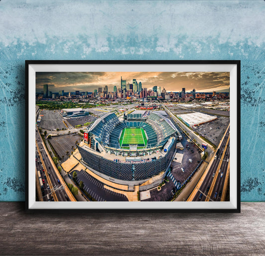 An aerial view of a large sports stadium surrounded by a city skyline, with the stadium's green field and surrounding parking lots visible.