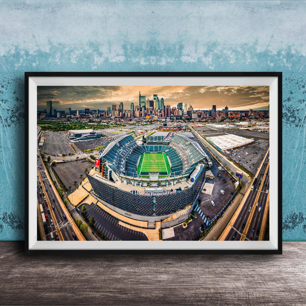 An aerial view of a large sports stadium surrounded by a city skyline, with the stadium's green field and surrounding parking lots visible.