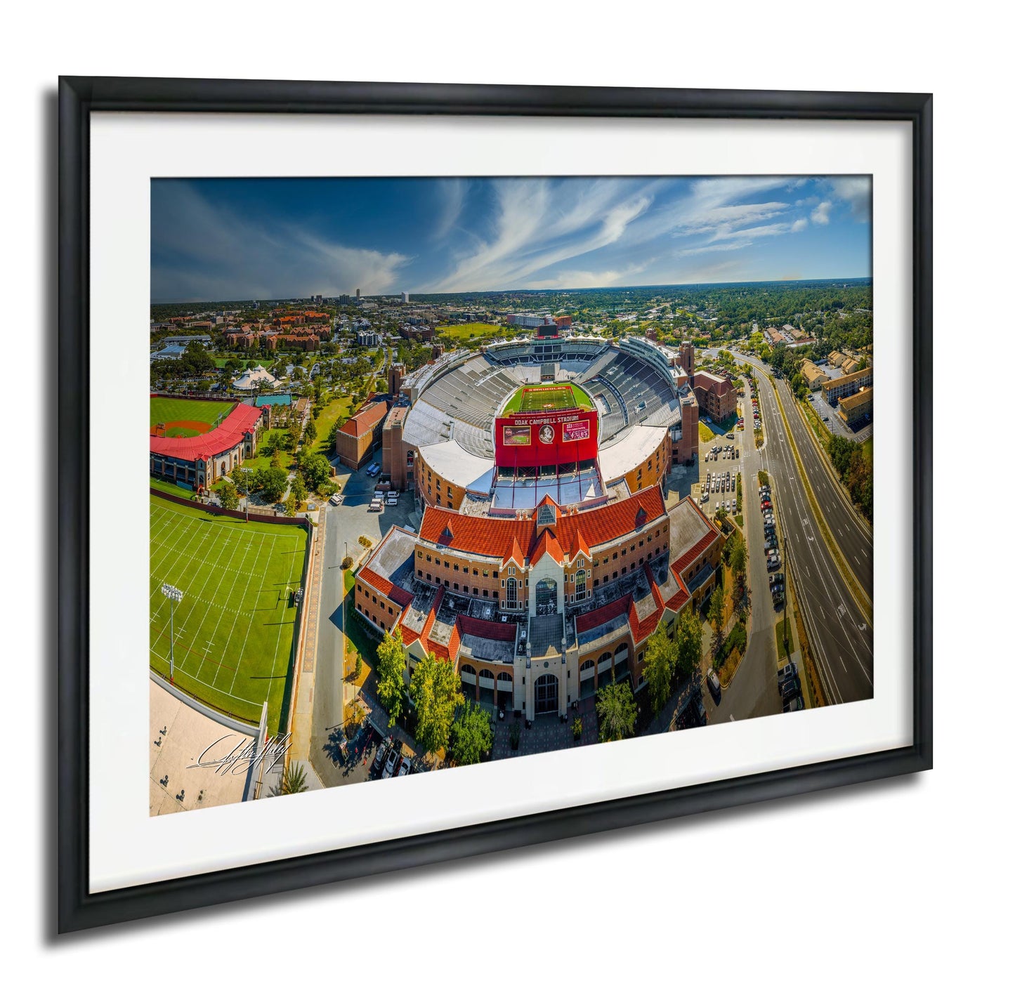 An aerial view of a large sports stadium with a red roof, surrounded by a cityscape with buildings, roads, and a tennis court.