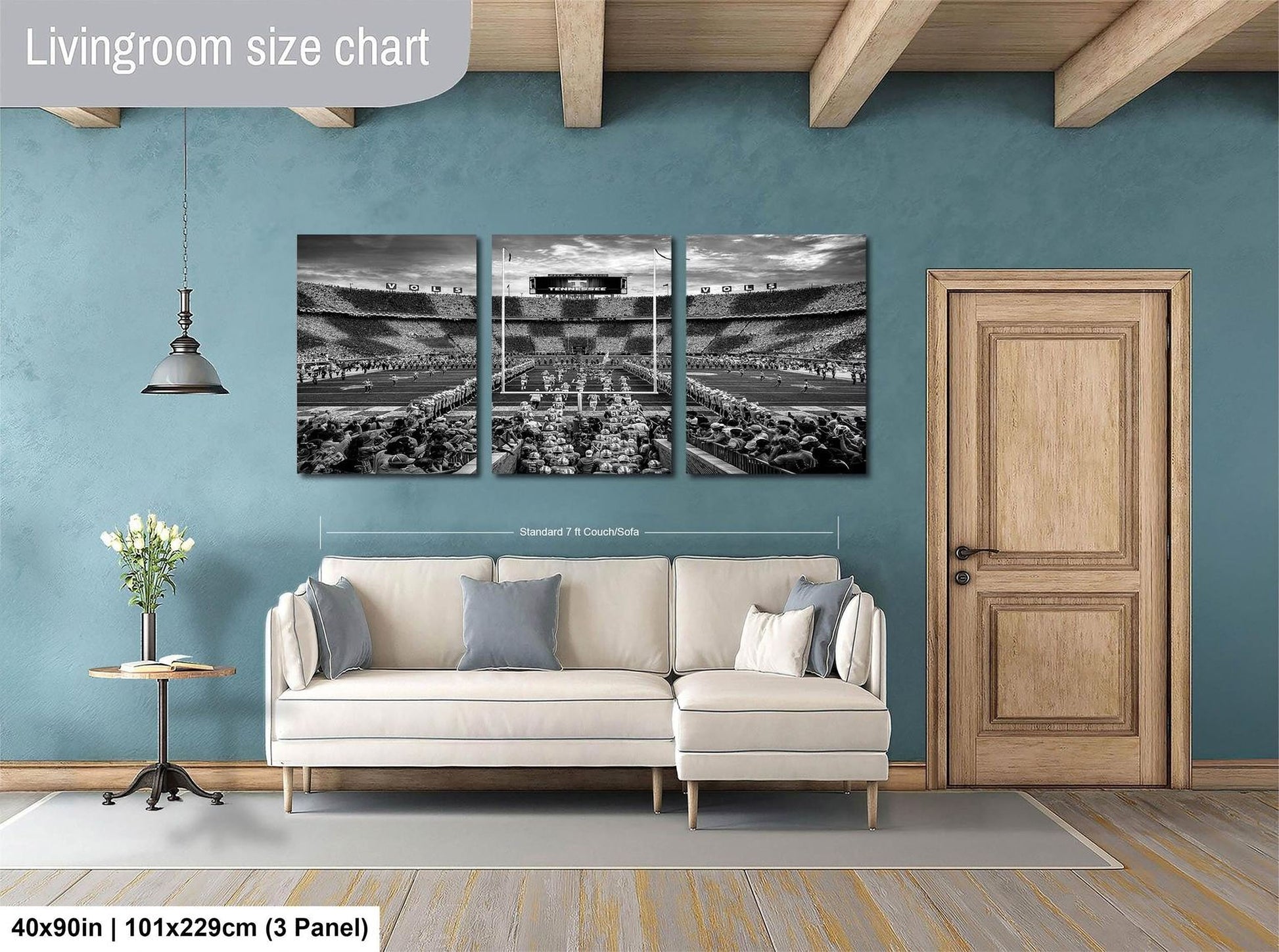 The image is a living room with a white sofa and a wooden door. Above the sofa, there is a large black and white photograph of a stadium, which appears to be a sports stadium. The photograph is divided into three panels, and the wall behind the sofa has a blue color. The living room is described as having a spacious and modern design, with a focus on the seating area and the large wall art.