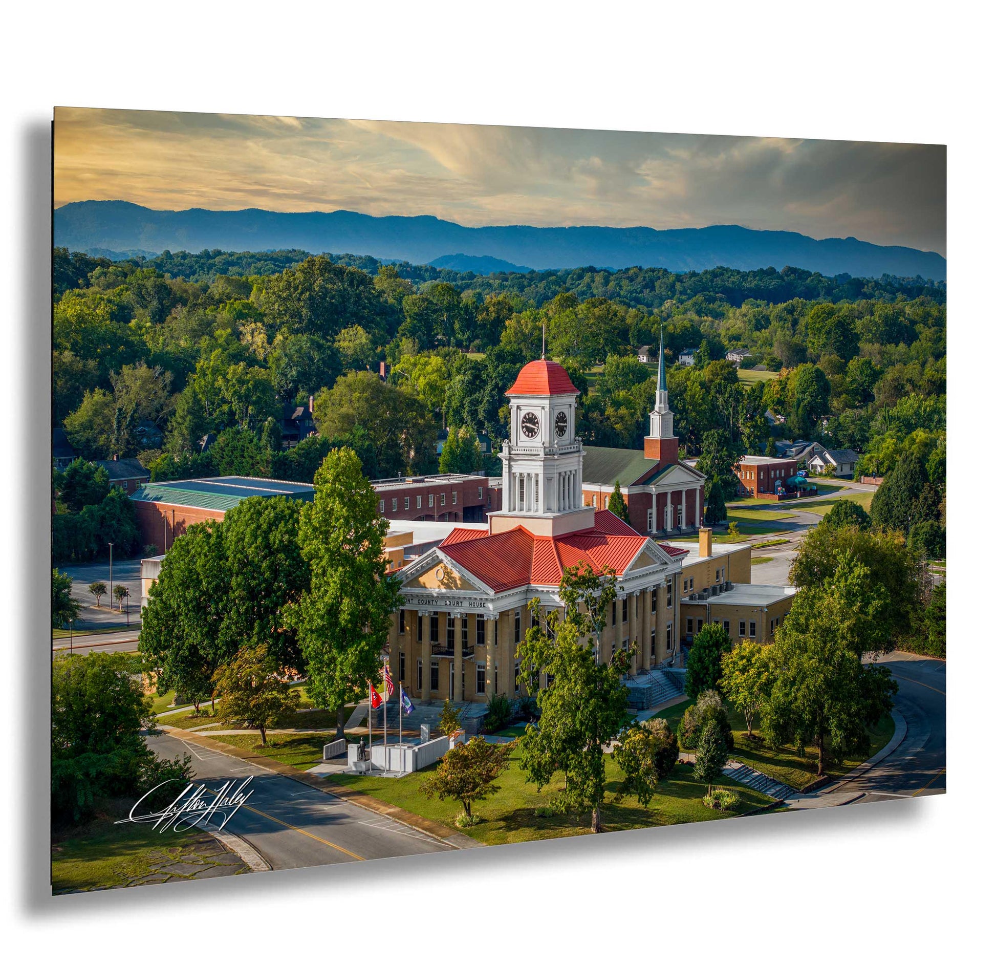 a large, ornate building with a red roof and a clock tower, surrounded by lush greenery and mountains in the background.