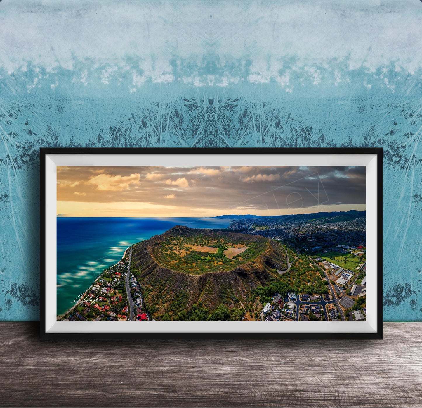 The image is a framed aerial view of a mountainous landscape with a coastal area, featuring a mix of green, brown, and blue colors.