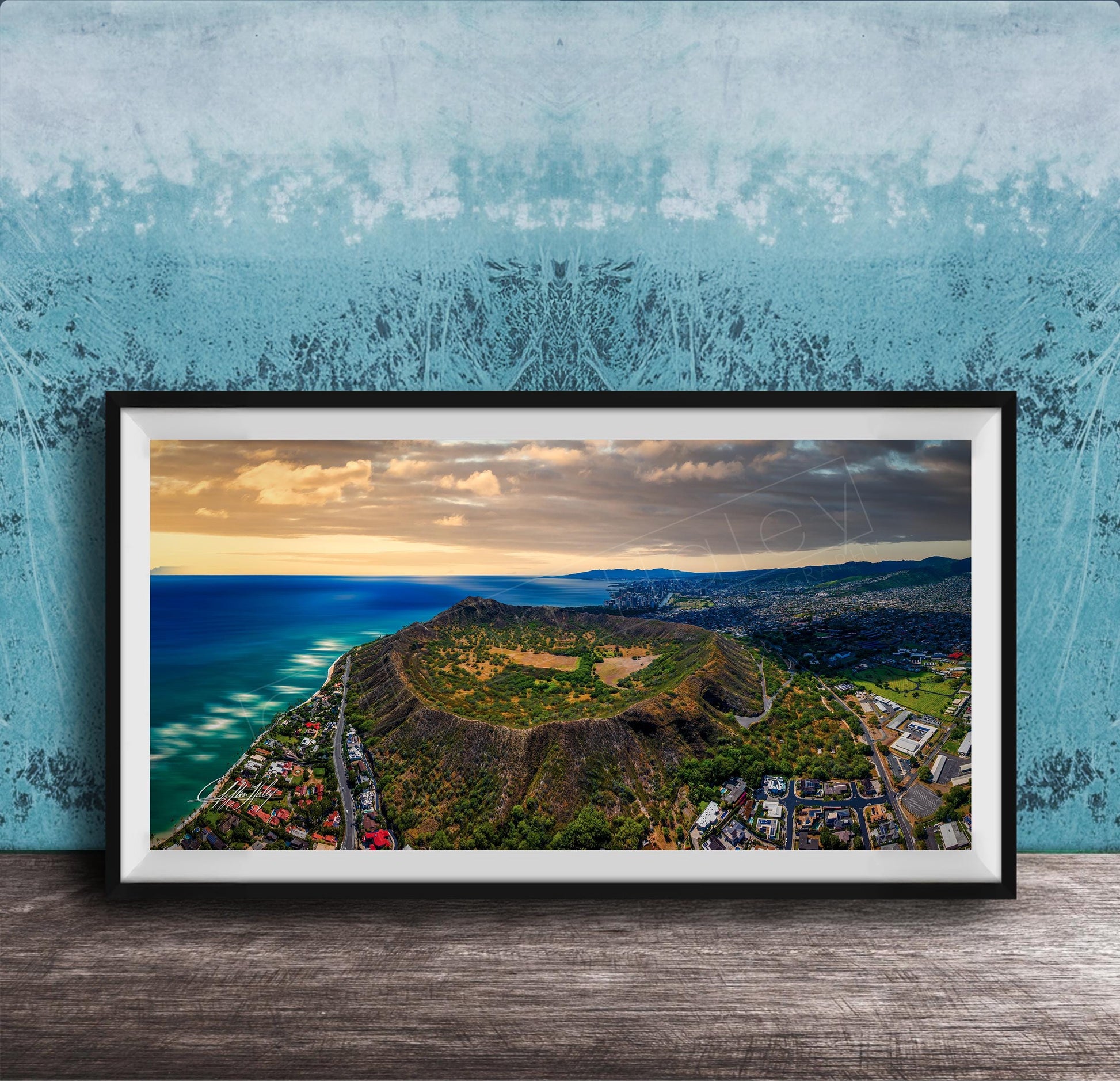 The image is a framed aerial view of a mountainous landscape with a coastal area, featuring a mix of green, brown, and blue colors.