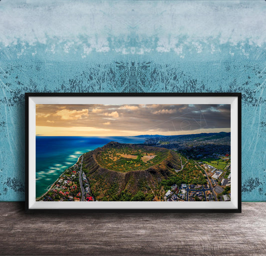 The image is a framed aerial view of a mountainous landscape with a coastal area, featuring a mix of green, brown, and blue colors.