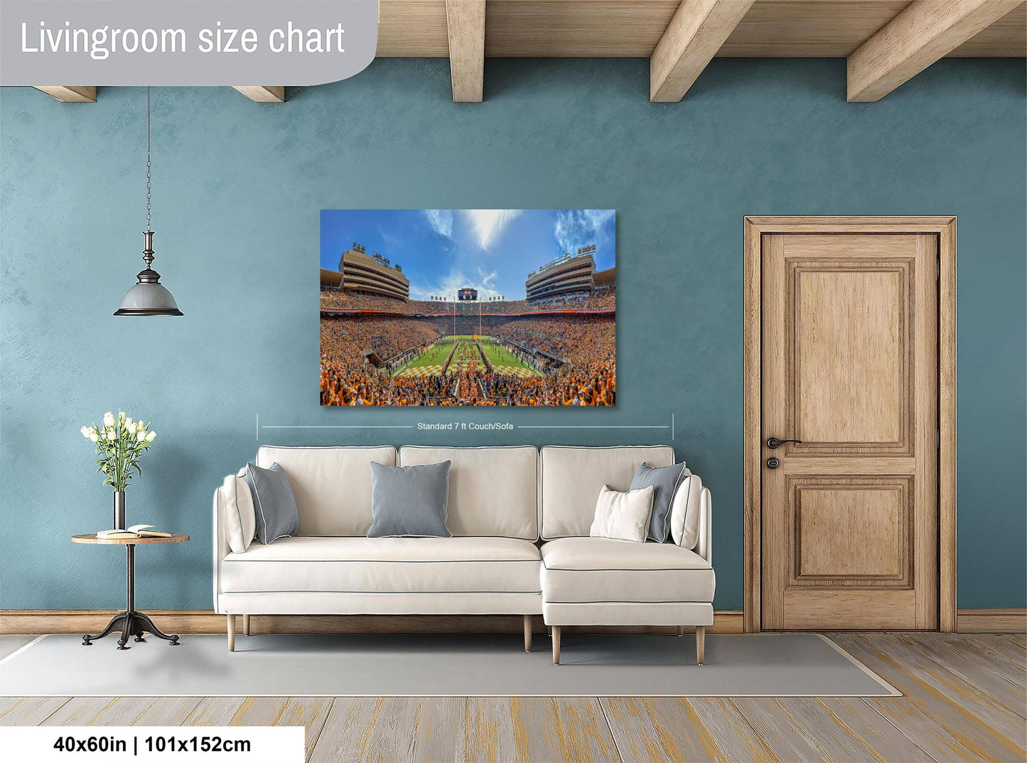 a living room with a large wall-mounted painting depicting a crowded stadium, a white sofa, a wooden door, and a small table with a vase of flowers.
