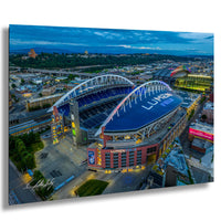 a large stadium with a curved roof, surrounded by a cityscape with buildings and roads. The stadium is brightly lit, and the sky above is blue with some clouds.
