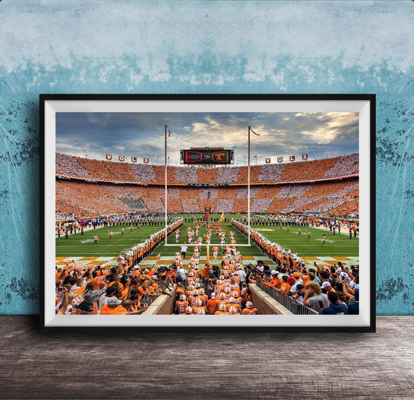 a large crowd of people gathered in a stadium, with a football field and players visible in the background.