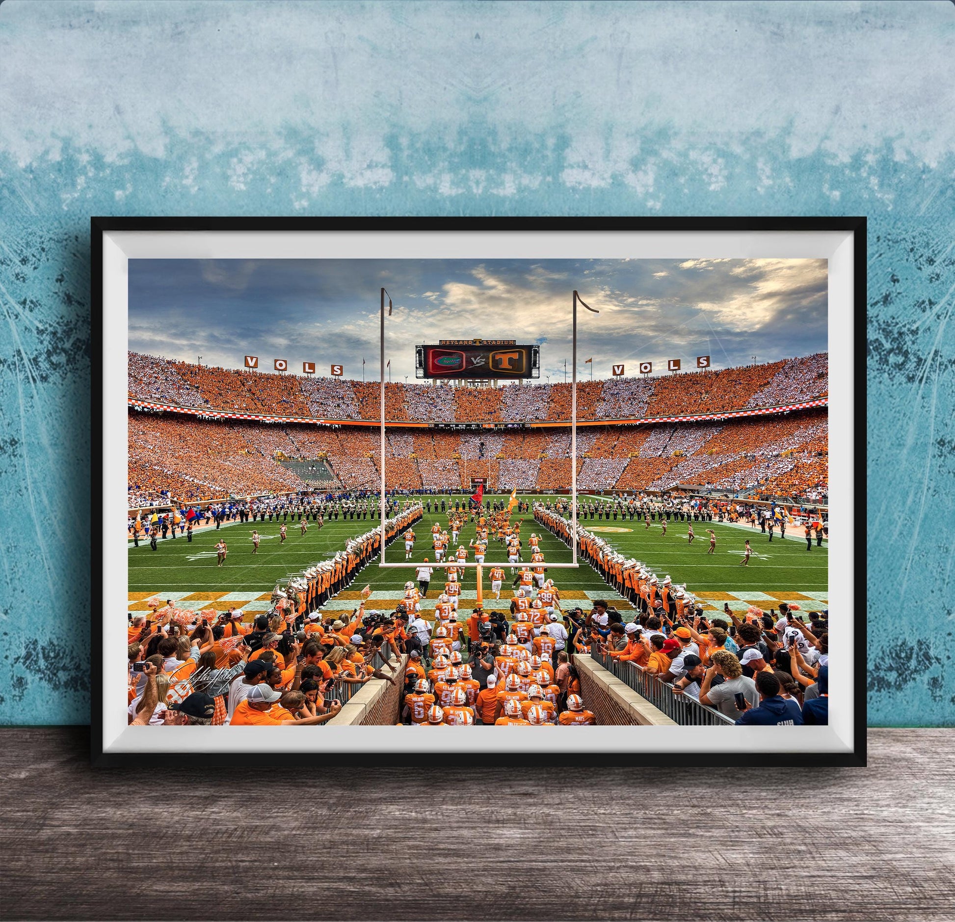 a large crowd of people gathered in a stadium, with a football field and players visible in the background.