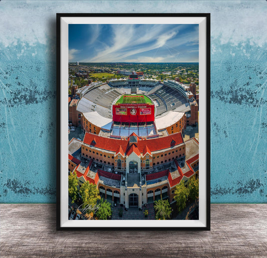 The image is an aerial view of a large stadium with a red roof, surrounded by buildings and a green field.