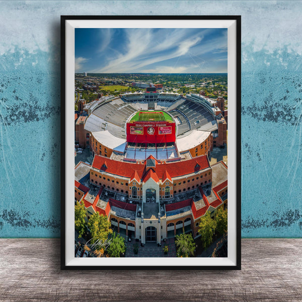 The image is an aerial view of a large stadium with a red roof, surrounded by buildings and a green field.