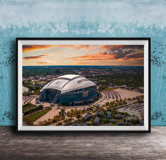 The image is a framed photograph of a large stadium with a curved roof, set against a backdrop of a city skyline and a colorful sunset sky.