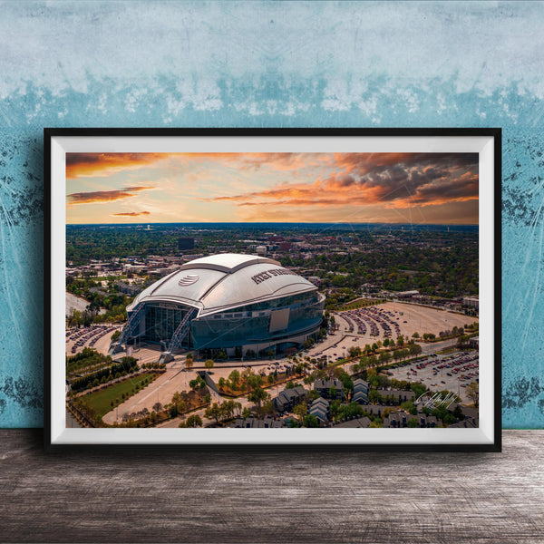 The image is a framed photograph of a large stadium with a curved roof, set against a backdrop of a city skyline and a colorful sunset sky.