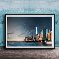 A framed photograph of the New York City skyline, with the One World Trade Center prominently visible, set against a blue sky with clouds.