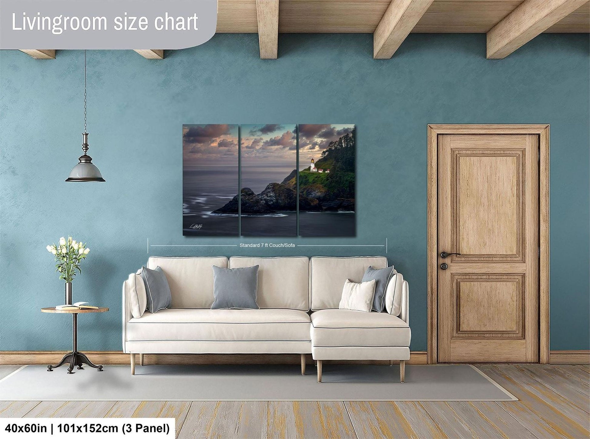 The image is a living room with a large painting of a coastal landscape hanging on the wall. The painting is divided into three panels, depicting a rocky coastline, a lighthouse, and a sunset over the ocean. The room has a white sofa and a wooden door, creating a cozy and inviting atmosphere.