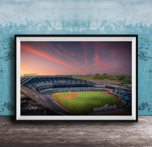 A framed photograph of a baseball stadium at sunset, with the field illuminated by the warm glow of the setting sun.