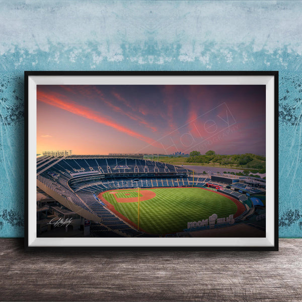 A framed photograph of a baseball stadium at sunset, with the field illuminated by the warm glow of the setting sun.
