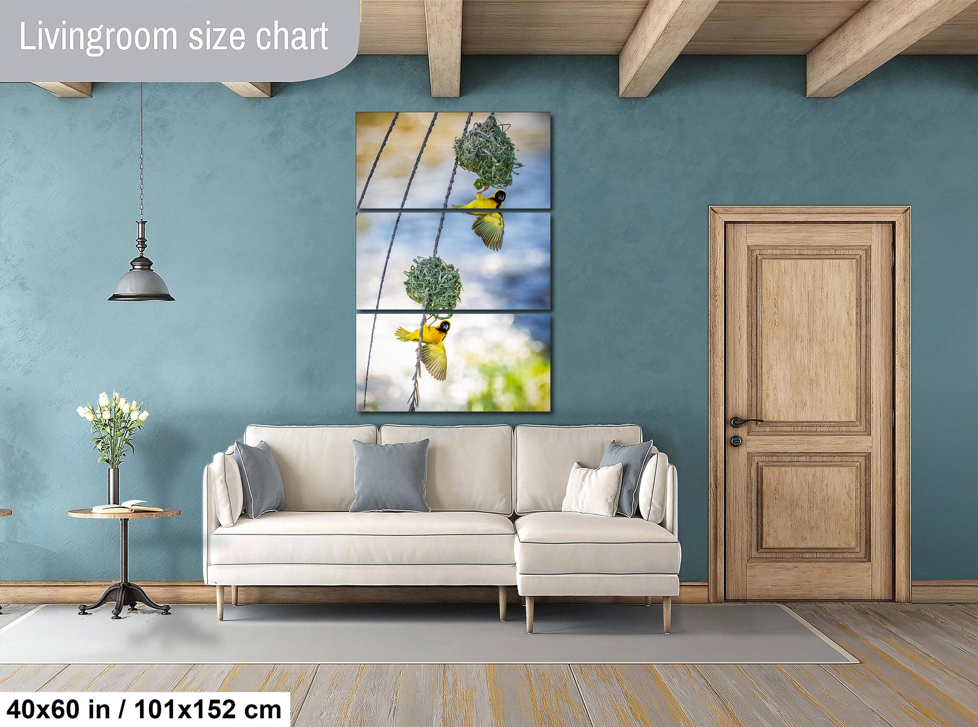 The image is a living room with a white sofa, a wooden door, and a large painting of birds hanging from a wire. The painting is a triptych, with two birds in the top and bottom panels and a bird in the middle panel. The room has a blue wall and a wooden floor, creating a cozy and inviting atmosphere.