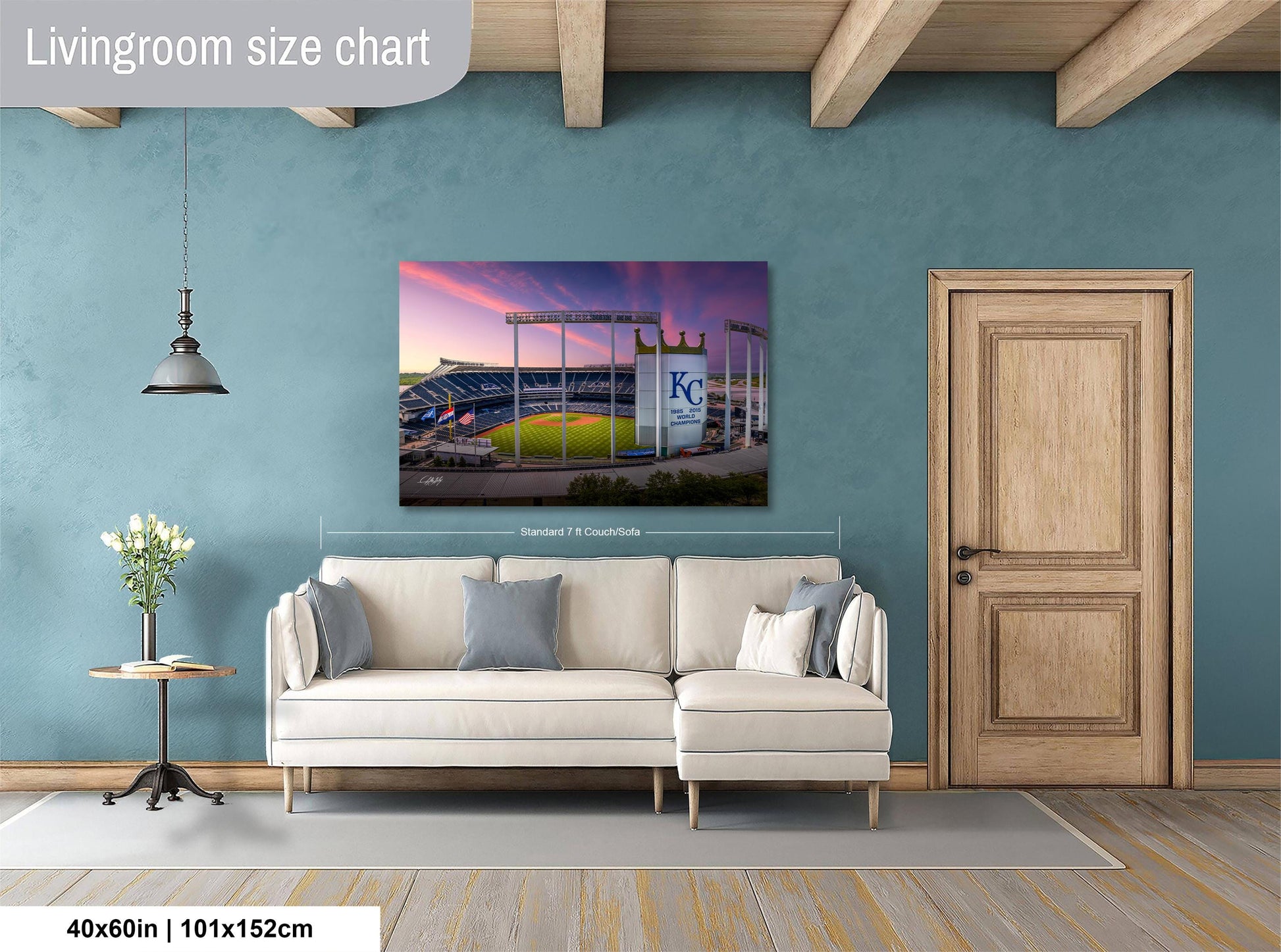 a living room with a large wall-mounted painting of a baseball stadium, a white sofa, a wooden door, and a small table with a vase of flowers.
