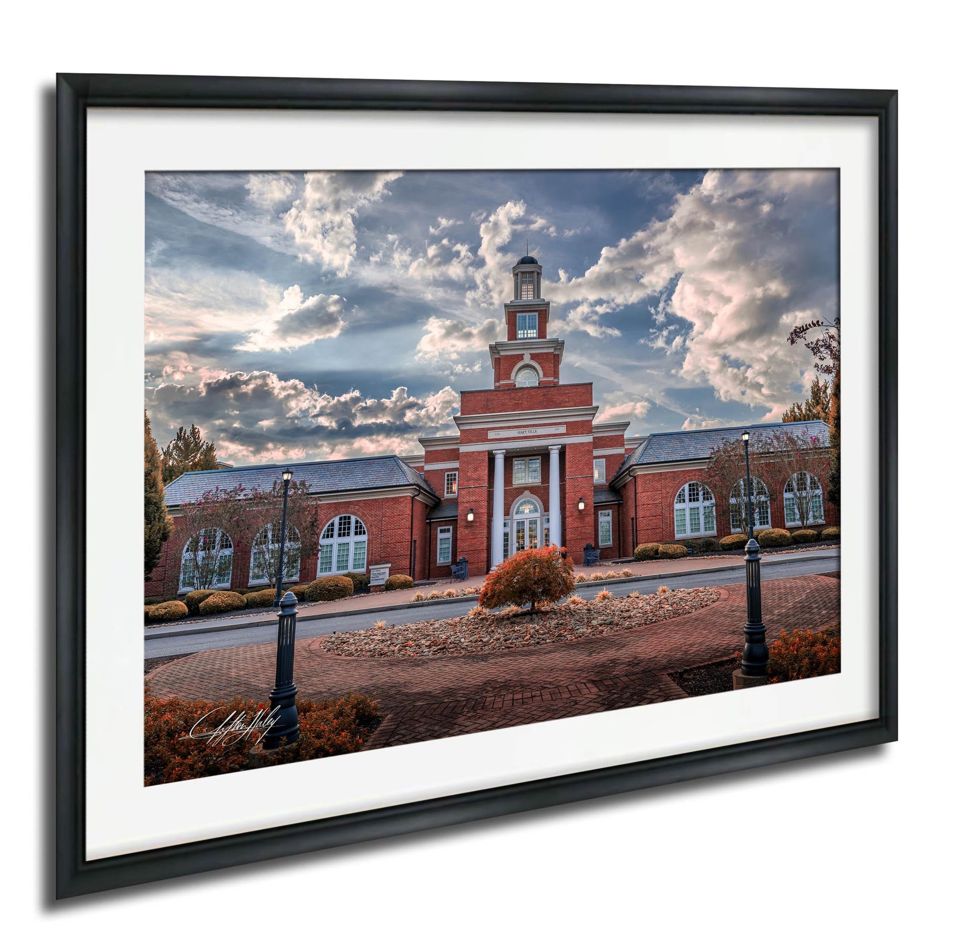 A framed photograph of a red brick building with a clock tower, surrounded by trees and a brick walkway.