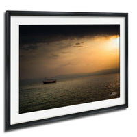 A boat is sailing on a calm body of water under a dramatic sky at sunset.