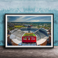 The image is a framed photograph of a football stadium, specifically Dokan Campbell Stadium, with a cityscape in the background.