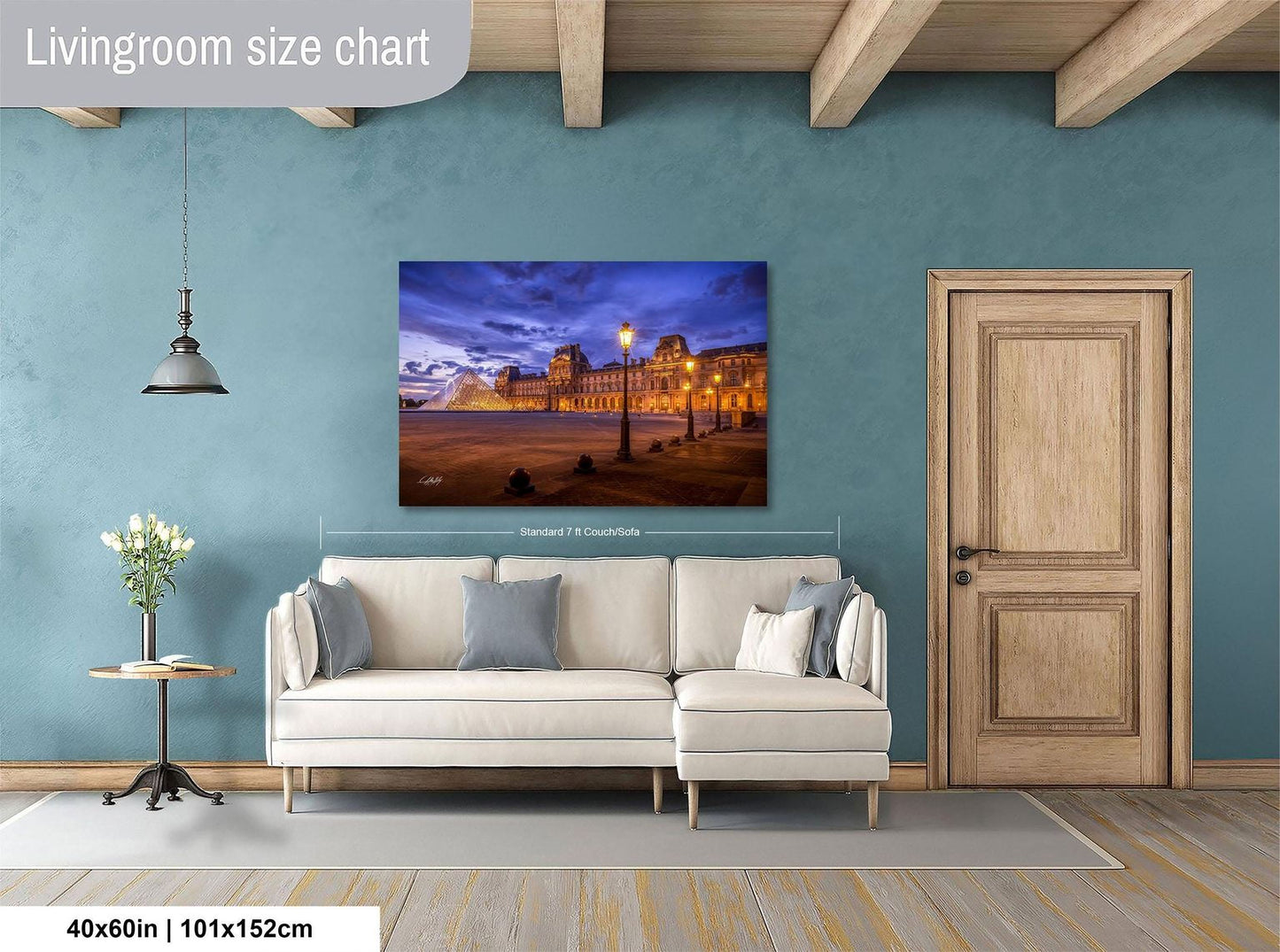 a living room with a large painting of a cityscape hanging on the wall. The painting is framed and measures 40 inches by 101.5 centimeters. The room has a white sofa, a wooden door, and a small table with a vase of flowers.