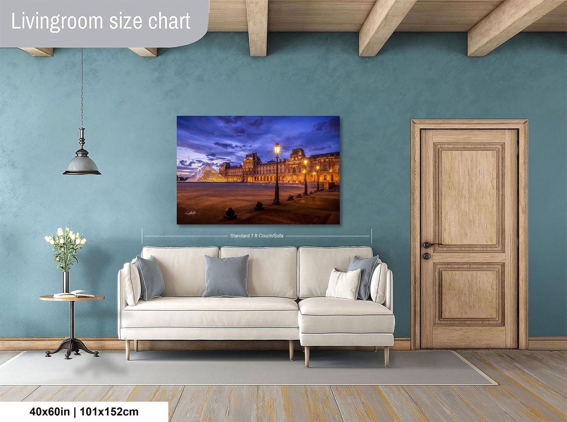 a living room with a large painting of a cityscape hanging on the wall. The painting is framed and measures 40 inches by 101.5 centimeters. The room has a white sofa, a wooden door, and a small table with a vase of flowers.
