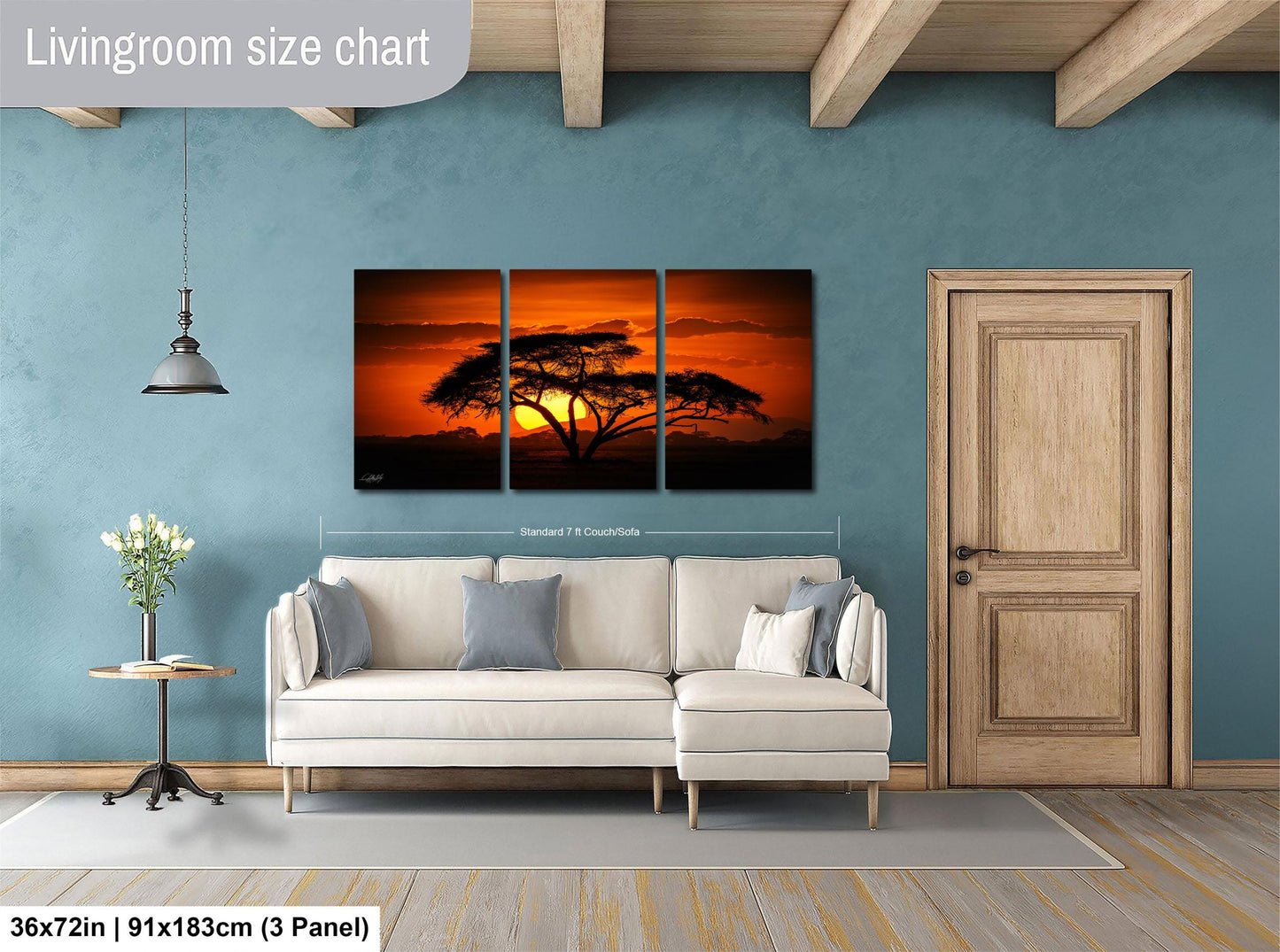 The image is a living room with a large wall art depicting a sunset over a tree. The wall art is divided into three panels, with the largest panel spanning approximately 36 square inches. The room also includes a white sofa, a wooden door, and a small table with a vase of flowers.