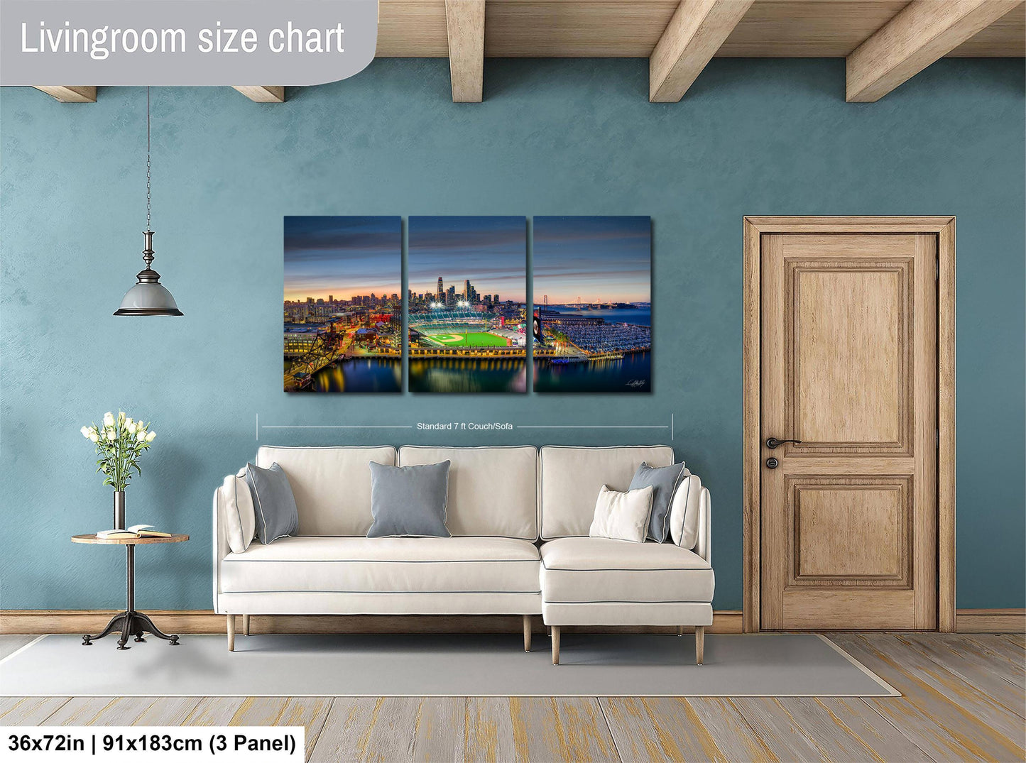 The image is a living room with a large wall art depicting a city skyline at night. The wall art is a collage of three panels, each showing a different view of the cityscape. The living room has a white sofa and a wooden door, and there is a potted plant and a vase on a table nearby. The wall art is approximately 36 inches wide and 9 inches tall, and it is mounted above the sofa.