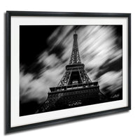 A black and white photograph of the Eiffel Tower in Paris, France, with a blurred background and a sense of motion.