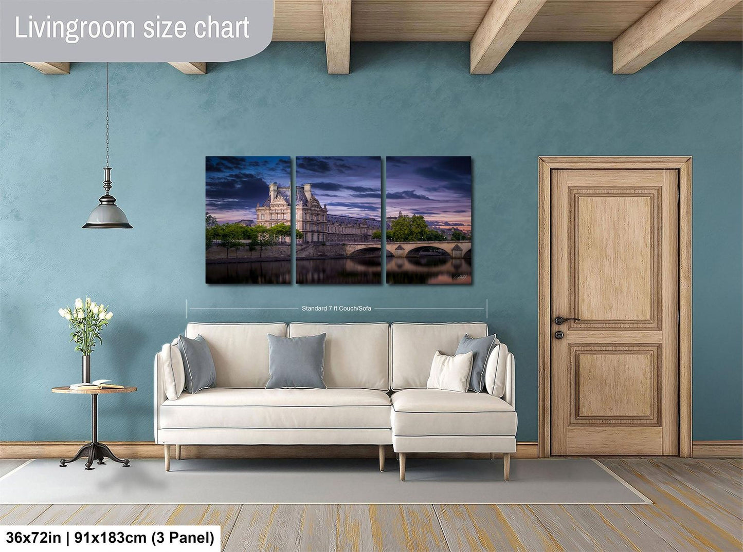The image is a living room with a large, three-piece wall art depicting a serene landscape with a castle and a river. The wall art is mounted above a white sofa, and there is a wooden door and a small table with a vase of flowers nearby. The living room appears to be well-lit and spacious, with a wooden ceiling and a rug on the floor.