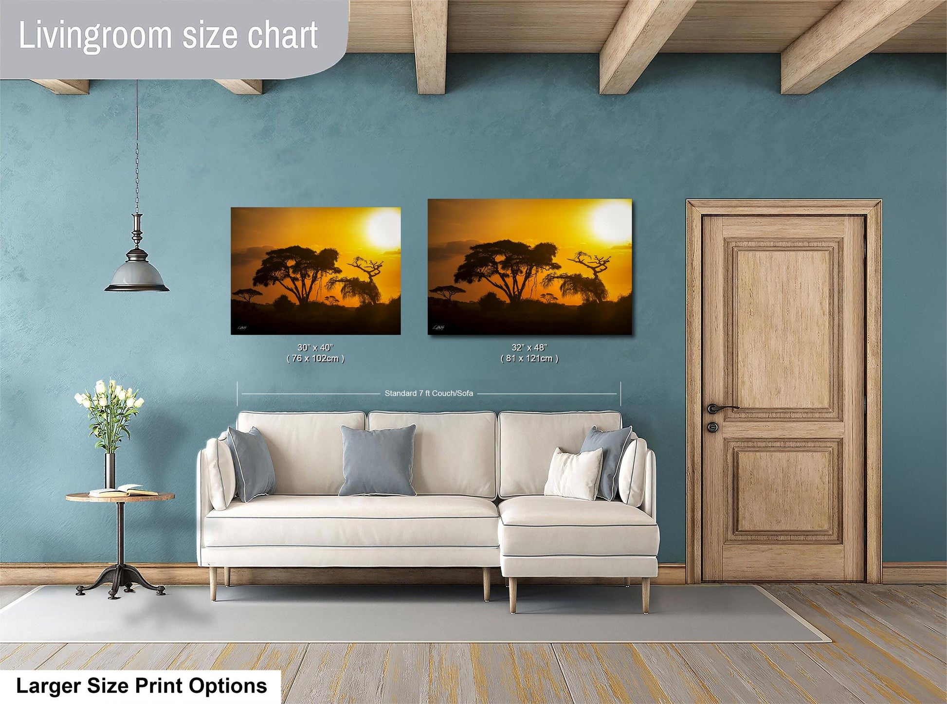a living room with a white sofa and a wooden door. Above the sofa, there are two framed pictures of a sunset landscape, with one picture being larger than the other. The living room has a blue wall and a wooden ceiling.