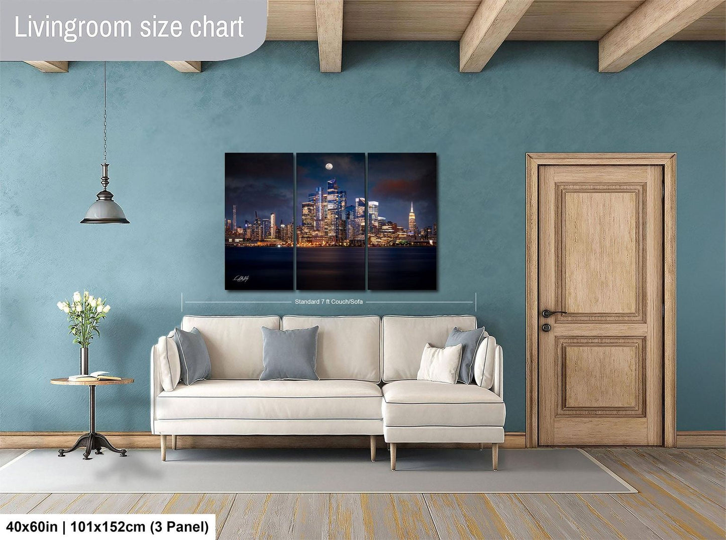 The image is a living room with a large, three-panel wall art depicting a city skyline at night. The wall art is mounted above a white sofa, and there is a wooden door and a small table with a vase of flowers nearby. The living room has a blue wall and wooden flooring.