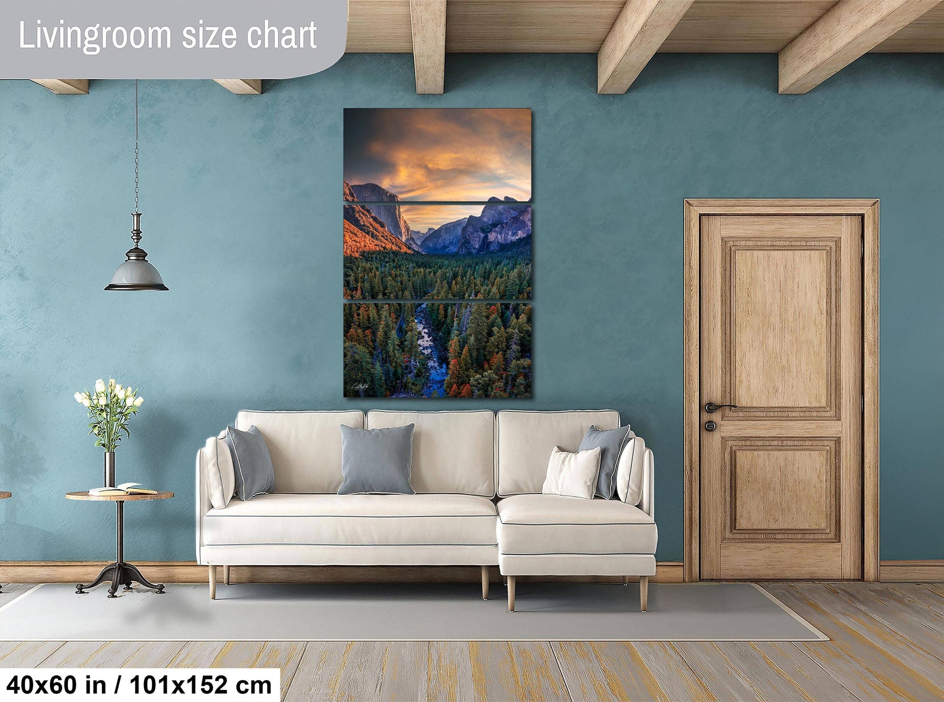 a living room with a large, colorful painting of a mountain landscape hanging on the wall. The painting is framed in a wooden frame and is approximately 40 inches wide and 51 inches tall. The room has a white sofa, a wooden door, and a small table with a vase of flowers.