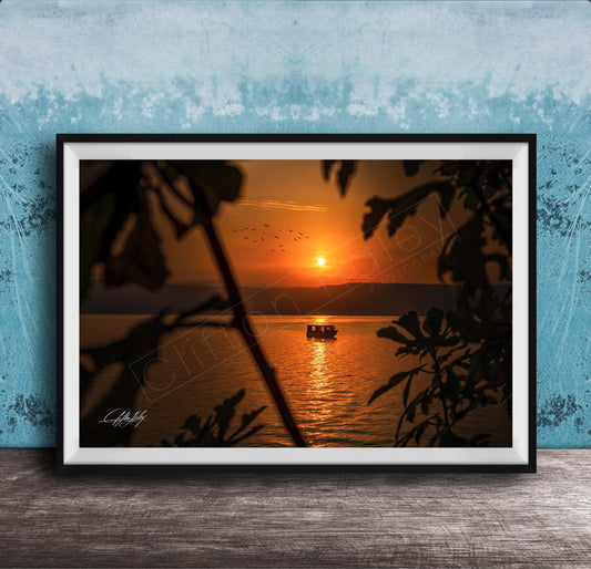 A framed photograph depicting a serene sunset over a body of water, with a small boat visible in the distance.