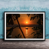 A framed photograph depicting a serene sunset over a body of water, with a small boat visible in the distance.