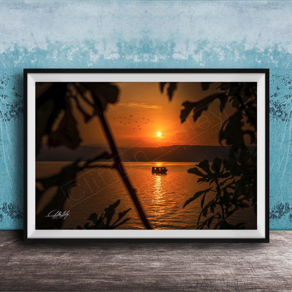 A framed photograph depicting a serene sunset over a body of water, with a small boat visible in the distance.