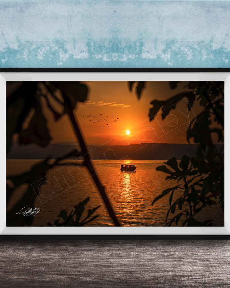 A framed photograph depicting a serene sunset over a body of water, with a small boat visible in the distance.