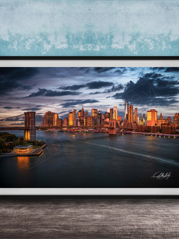 A framed photograph of the New York City skyline at dusk, with the city's iconic landmarks and buildings illuminated against a dramatic cloudy sky.