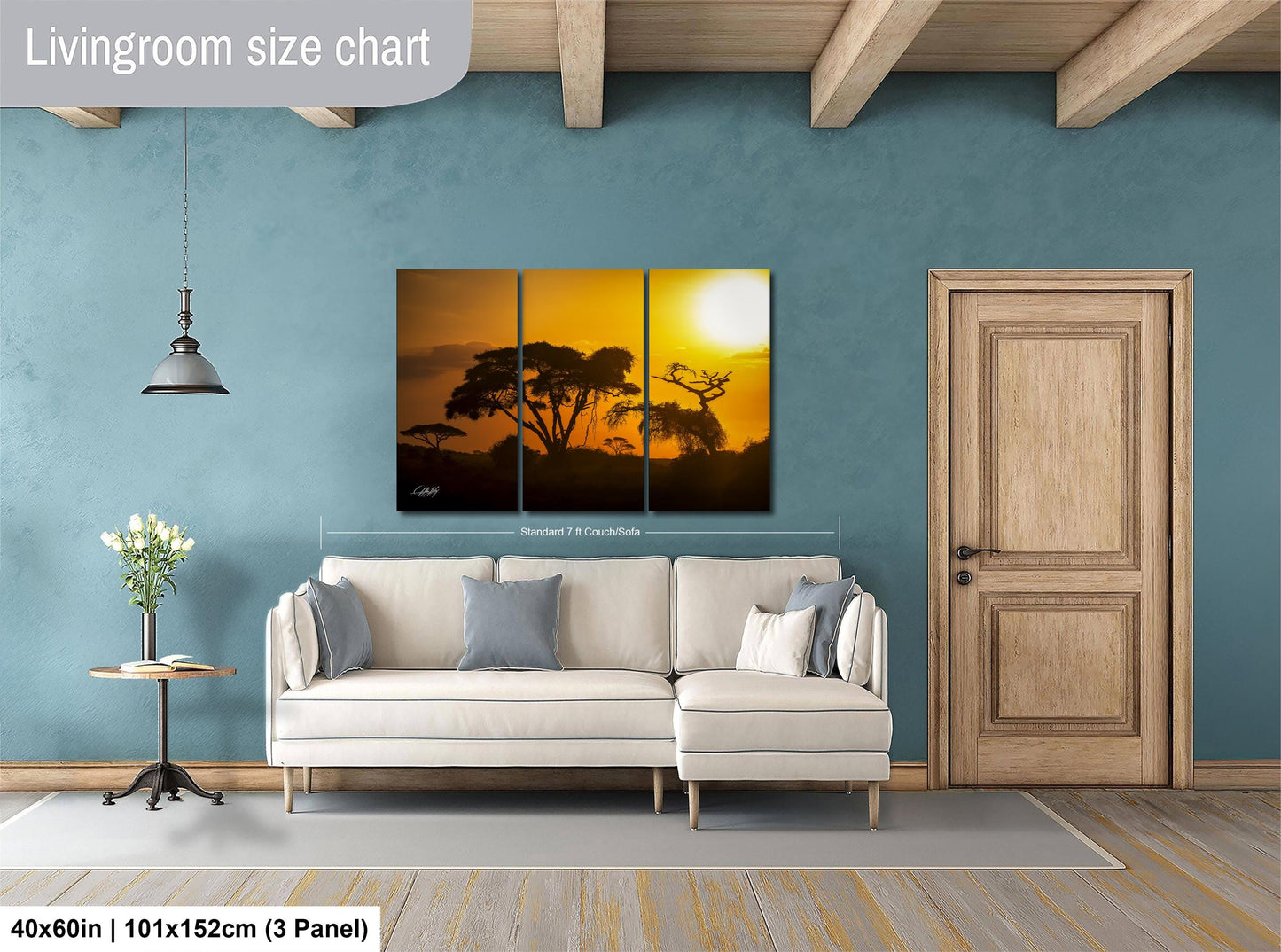 The image is a living room with a large, three-panel landscape painting hanging on the wall. The painting depicts a sunset over a field of trees. The room has a white sofa, a wooden door, and a small table with a vase of flowers. The painting is approximately 40 inches wide and 101 inches tall, with a 3-panel layout.