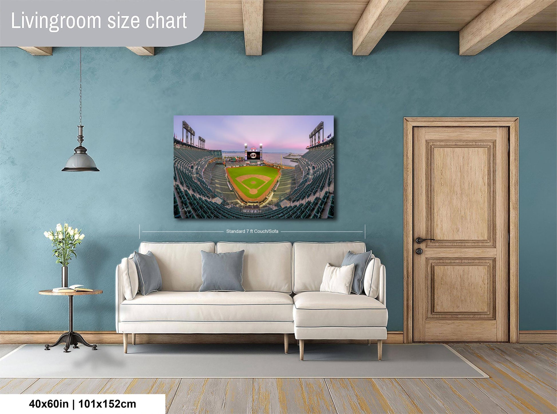 a living room with a large wall-mounted painting depicting a baseball stadium. The painting is framed and hangs above a white sofa, which is positioned in front of a wooden door. The room has a wooden floor and a small table with a vase of flowers. The painting is approximately 40 inches wide and 115 centimeters tall.
