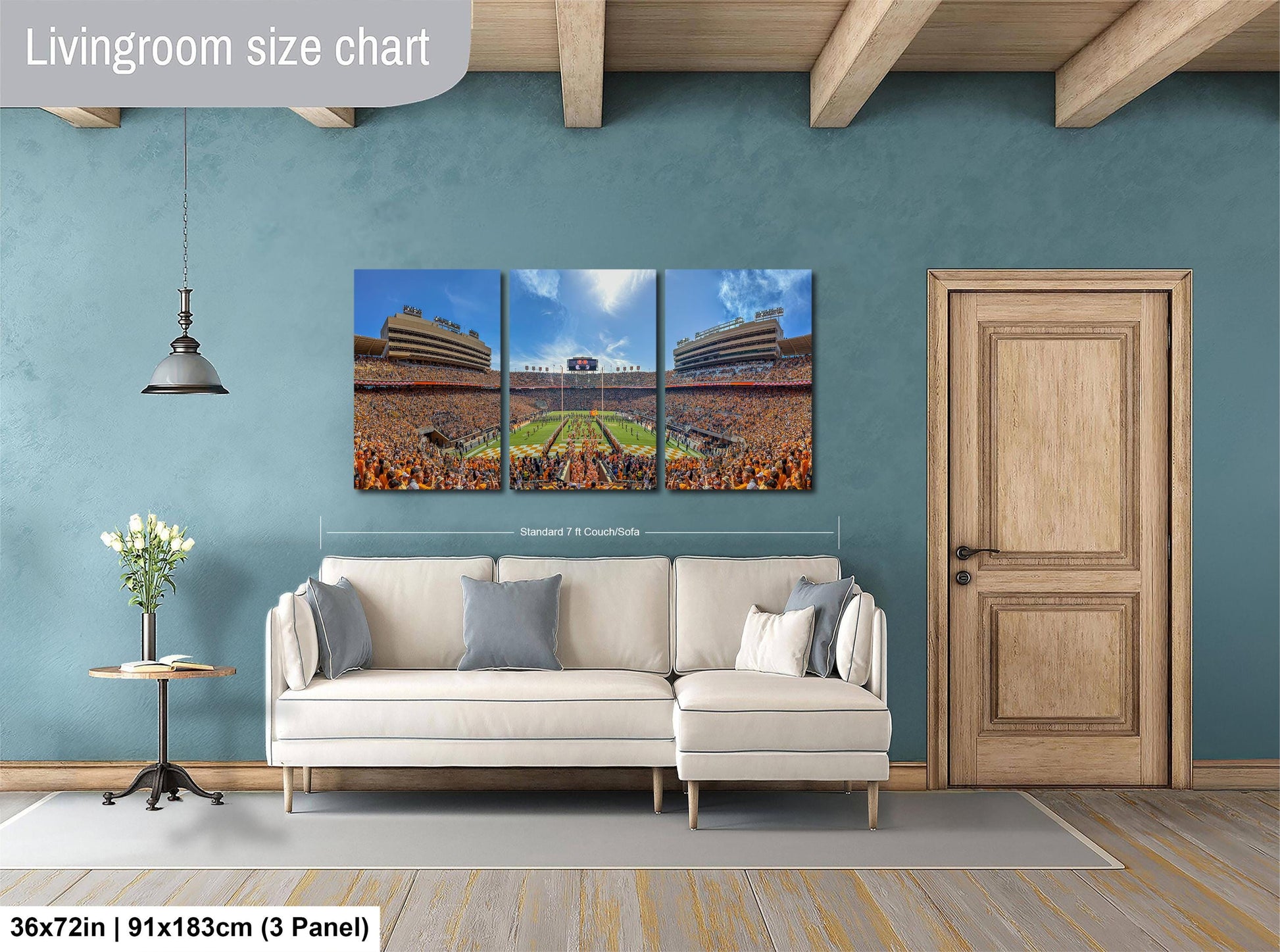 The image is a living room with a large wall art depicting a stadium scene. The wall art is a collage of three panels, each showing different aspects of the stadium. The living room has a white sofa and a wooden door, and there is a potted plant and a vase on a table nearby. The wall art is approximately 36 inches wide and 9 inches tall, and it is mounted on a blue wall.